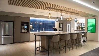 Modern office break room with a large island, bar seating, pendant lighting, stainless steel appliances, blue tile backsplash, and collaborative gathering space.
