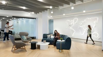 Contemporary office lounge with flexible seating, collaborative meeting areas, a backlit world map feature wall, and employees working and moving throughout the space.