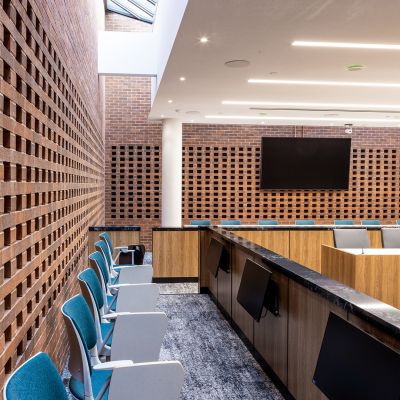 Corner of a mock trial room with brick walls, student seats, and monitirs.