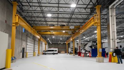 Interior of a newly constructed industrial service facility with high-bay space, overhead bridge cranes, polished concrete floors, large overhead doors, and service vehicles and equipment positioned beneath the crane system.