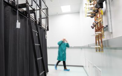 Controlled laboratory environment with dark black curtains enclosed around a secure testing table. A technician wearing cleanroom garments is walking around the corner of the room.