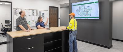 Three employees reviewing an interactive outage map displayed on a large wall-mounted screen in an office setting.