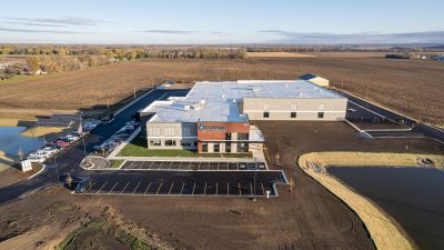 Aerial view of the Agralite Electric Cooperative headquarters under construction, surrounded by farmland, with parking lot and solar panels visible.