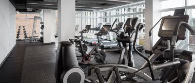 Bright office fitness center with cardio equipment, free weights, and large windows overlooking the city.