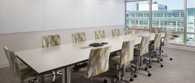 Modern conference room with a long meeting table, patterned chairs, and floor-to-ceiling windows.