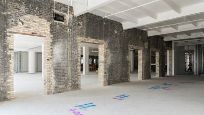 A partially restored brick interior with large openings and colorful markings on the floor.