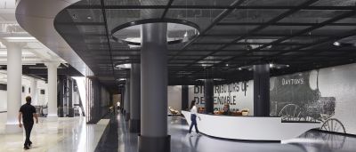 Lobby with black mesh ceiling, dark columns, and a curved white reception desk beneath a "Dayton's" mosaic wall mural.