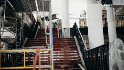 Workers in safety vests walk down a rust-colored construction staircase inside an unfinished building.