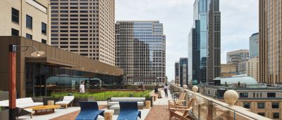 Rooftop terrace with wood decking, blue lounge chairs, and sofas surrounded by downtown high-rises.