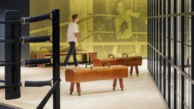 Gym area with leather pommel horses, hanging punching bag, and a mustard-yellow mesh wall with a vintage photo graphic.