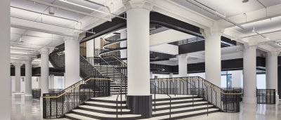 Grand black-and-white staircase with patterned metal railings beneath ornate white columns in a renovated historic building.
