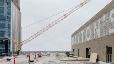 Rooftop view of a construction crane beside a weathered brick wall with faded "Dayton's" signage.