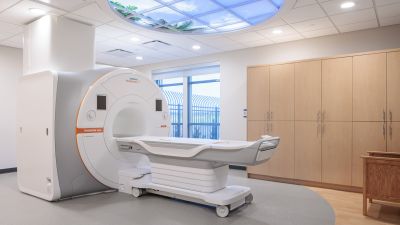 An MRI room with a Siemens scanner beneath a decorative skylight-style ceiling panel depicting palm trees and sky.