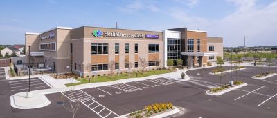 Exterior view of a HealthPartners Clinic Urgent Care building with a landscaped parking lot under a blue sky.
