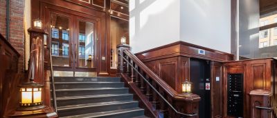 Historic entrance with dark wood paneling, antique lantern-style light fixtures, an elevator, and mailboxes beside a staircase.