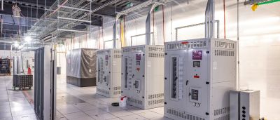 Rows of large electrical switchgear cabinets in a data center under construction, with wrapped equipment and cable trays overhead.