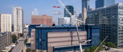 A tall crane hoists rooftop mechanical equipment above a mid-rise building amid the downtown Minneapolis skyline.