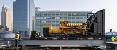 A yellow industrial generator with visible engine components sits on a rooftop platform, framed by downtown skyscrapers.