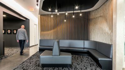 A man walks past a curved wood-slat lounge nook with a leather bench seat and framed staff portraits.