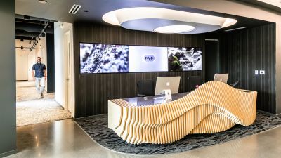 A wave-like wood reception desk with dual computer monitors, set below a video wall displaying the OVO logo.
